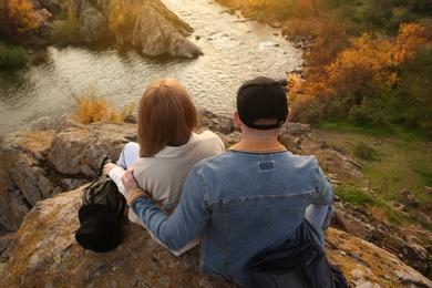 Couple of hikers with travel backpacks sitting on steep cliff, above view