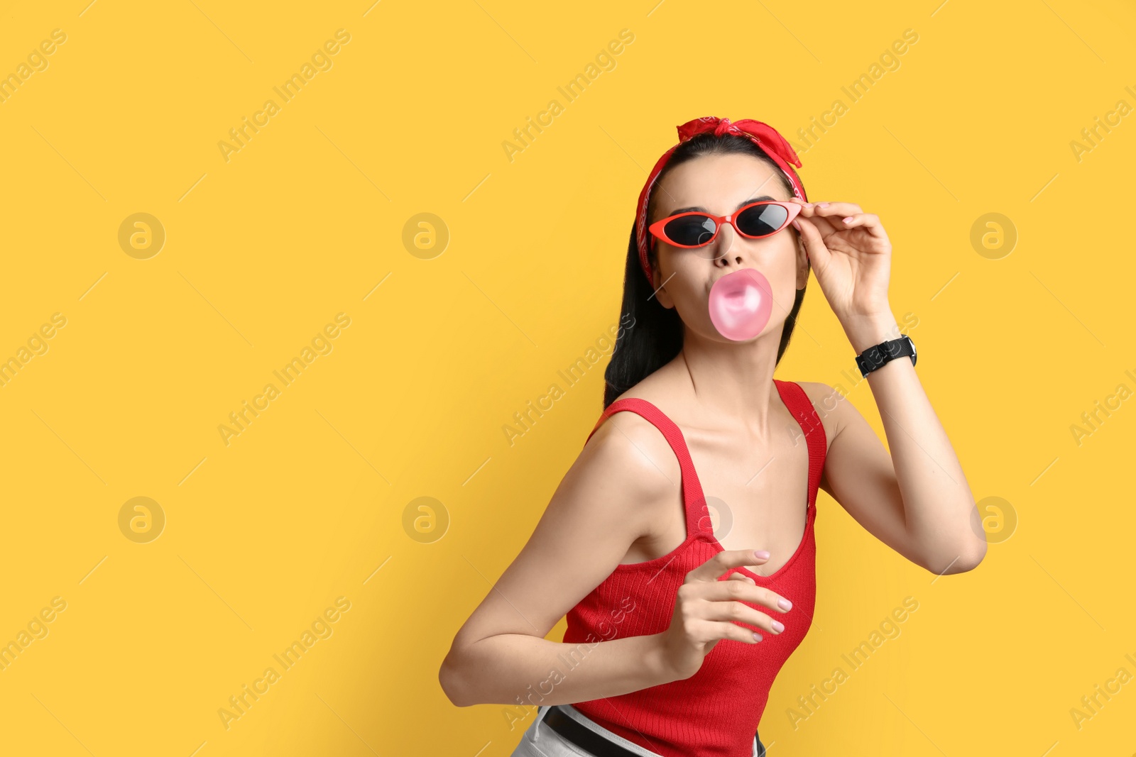 Photo of Fashionable young woman in pin up outfit blowing bubblegum on yellow background, space for text