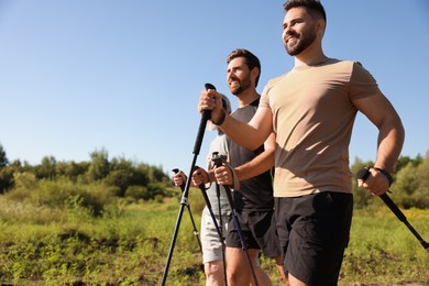 Happy men practicing Nordic walking with poles outdoors on sunny day