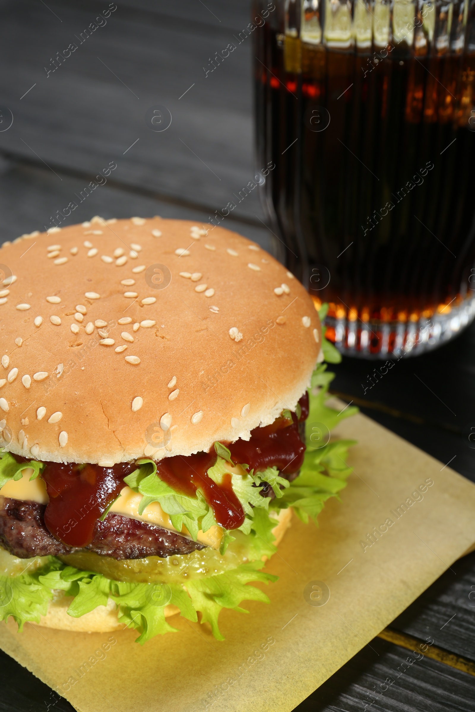 Photo of Burger with delicious patty and soda drink on black wooden table