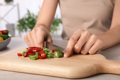 Photo of Woman cutting chili peppers at table, closeup