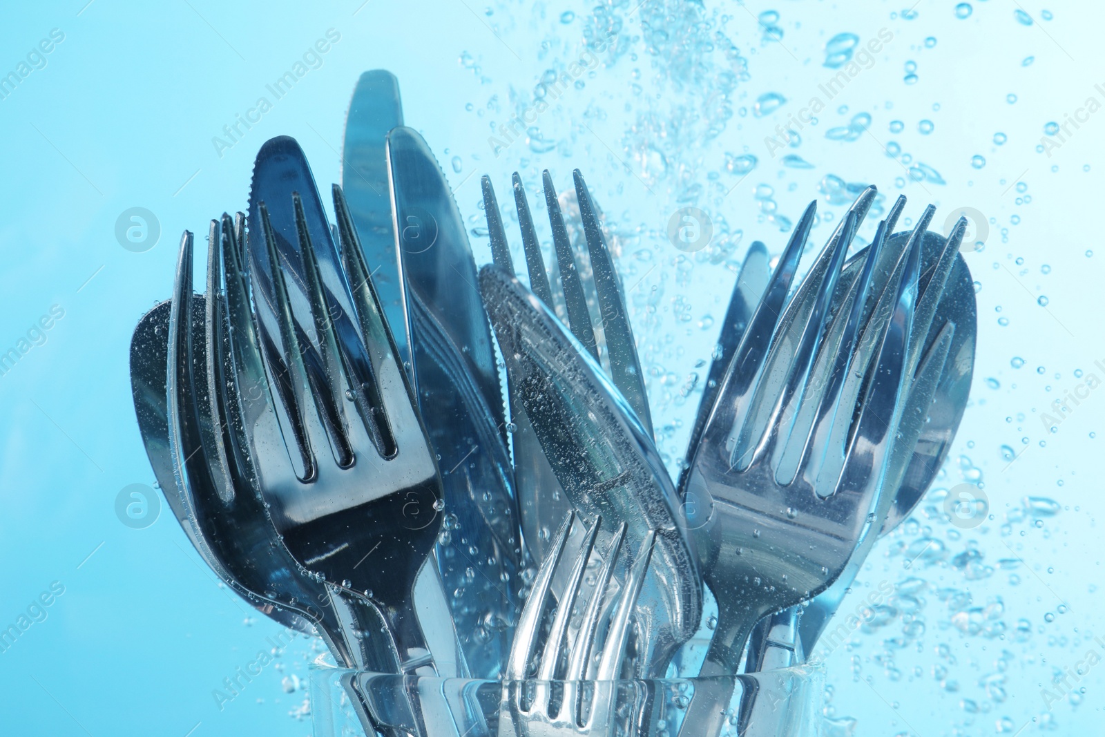 Photo of Washing silver cutlery in water on light blue background