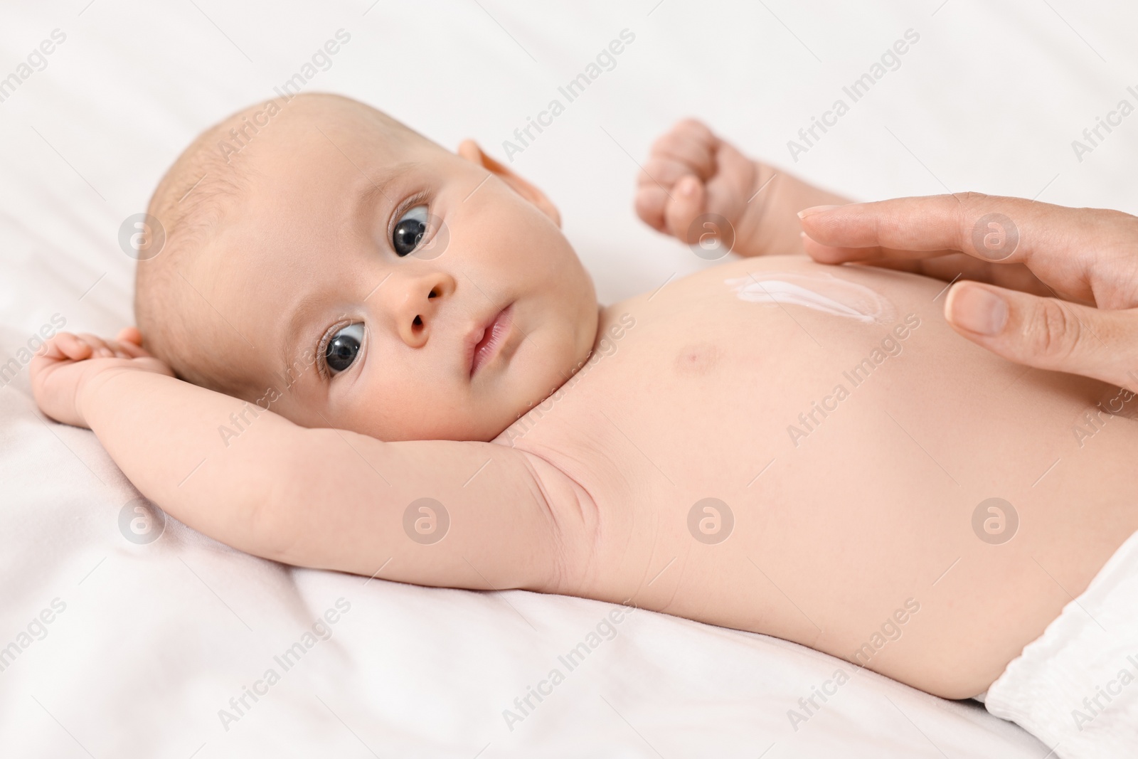 Photo of Woman applying body cream onto baby`s skin on bed, closeup