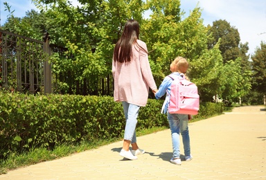 Young mother taking her little child to school through park