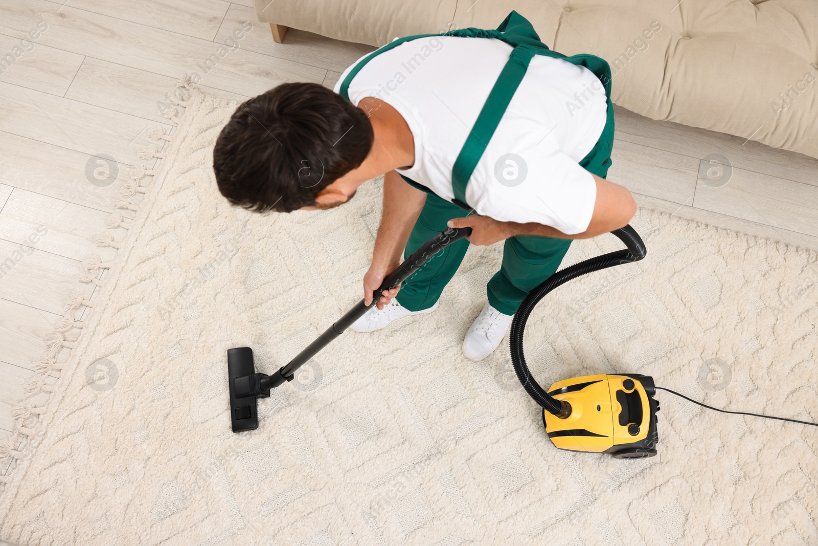 Photo of Dry cleaner's employee hoovering carpet with vacuum cleaner indoors, above view