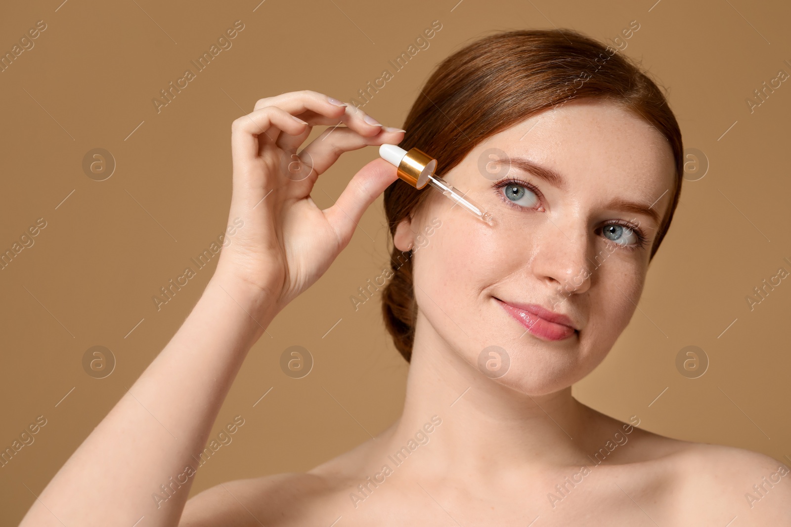 Photo of Beautiful woman with freckles applying cosmetic serum onto her face on beige background