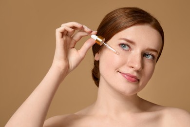 Beautiful woman with freckles applying cosmetic serum onto her face on beige background