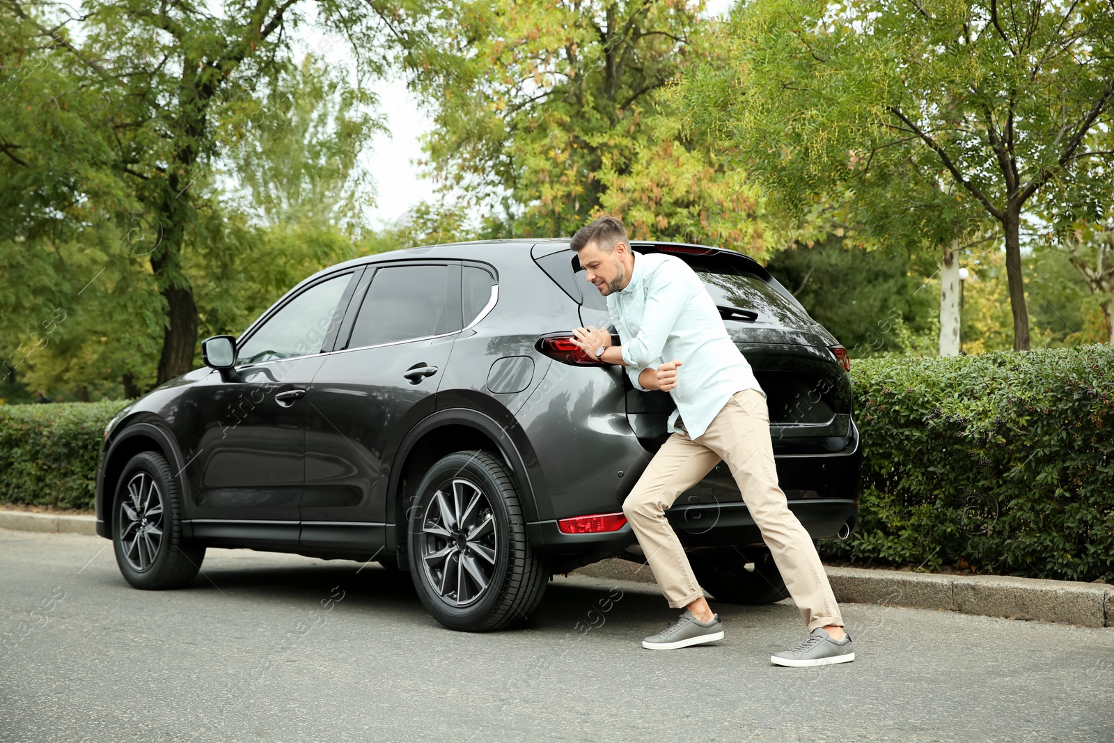 Photo of Man pushing broken car on road along city street