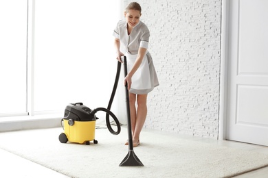 Photo of Chambermaid cleaning carpet with vacuum  indoors