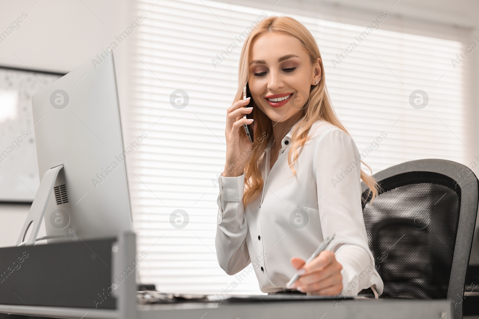 Photo of Secretary talking on smartphone at table in office