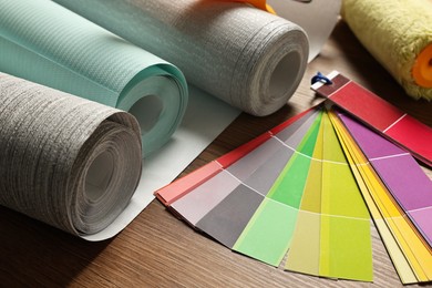 Photo of Different wallpaper rolls and color palette samples on wooden table, closeup