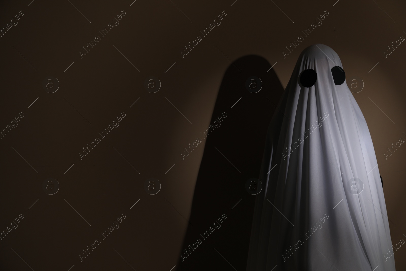 Photo of Creepy ghost. Woman covered with sheet on brown background, space for text