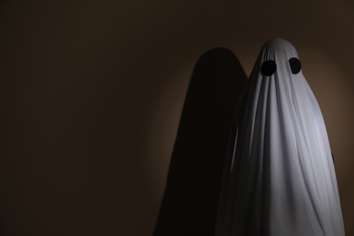 Photo of Creepy ghost. Woman covered with sheet on brown background, space for text