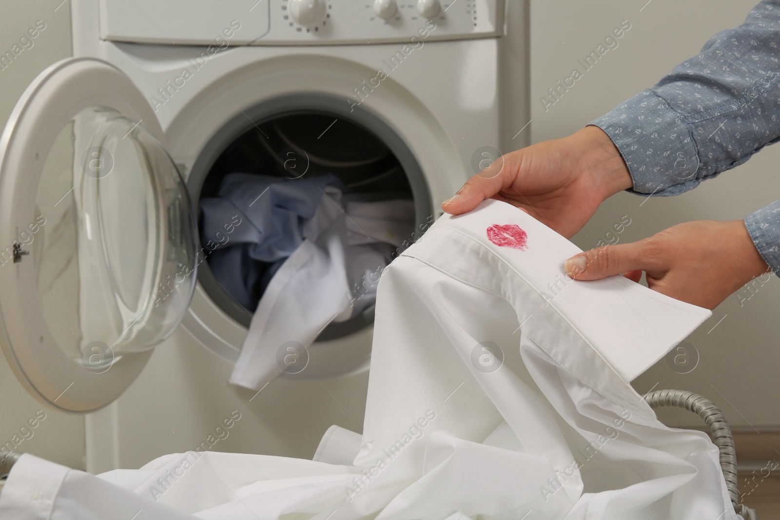 Photo of Woman holding her husband's shirt with lipstick kiss mark indoors, closeup