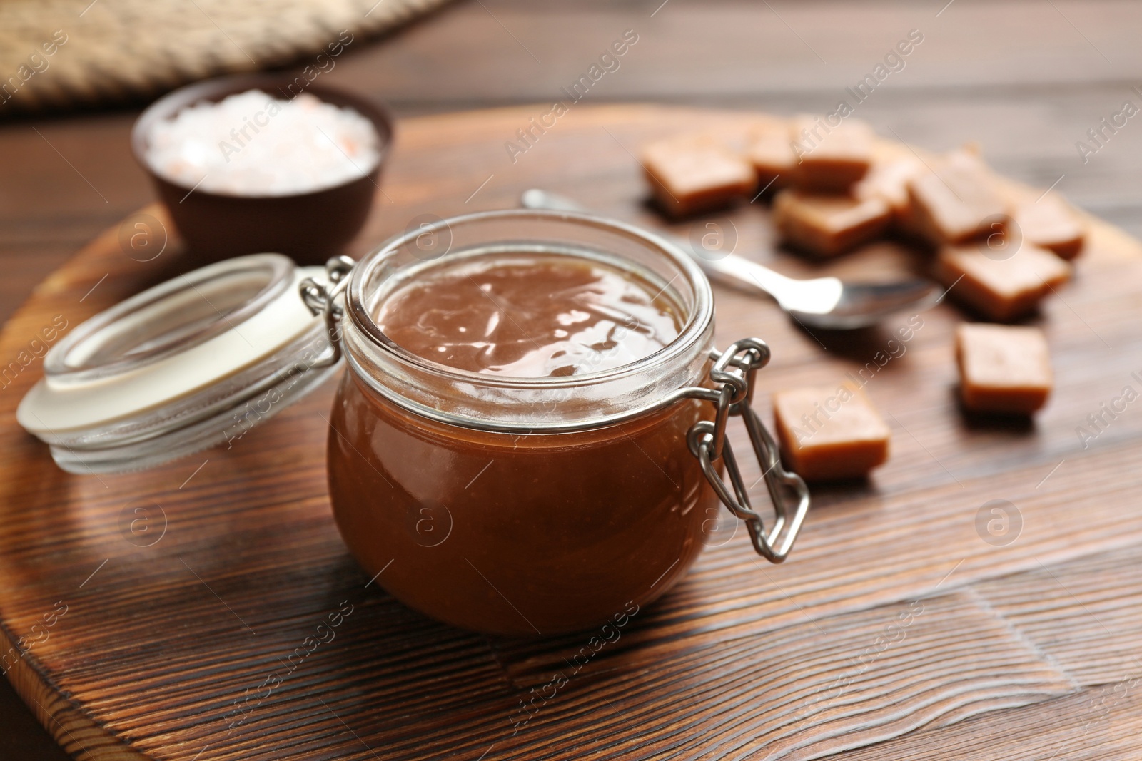 Photo of Jar of tasty caramel sauce on board, closeup