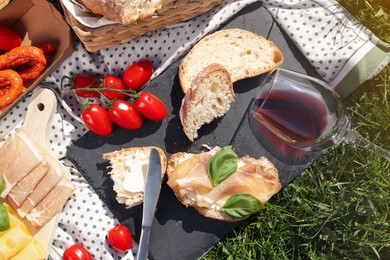 Blanket with wine and snacks for picnic on green grass, flat lay