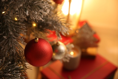 Red bauble hanging on Christmas tree indoors, space for text