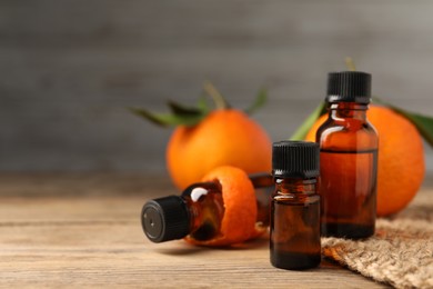 Photo of Bottles of tangerine essential oil, fresh fruit and peel on wooden table, closeup. Space for text