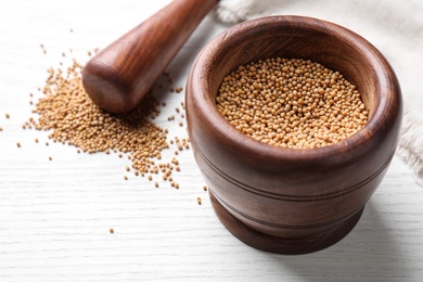 Mustard seeds with wooden mortar and pestle on white table, closeup