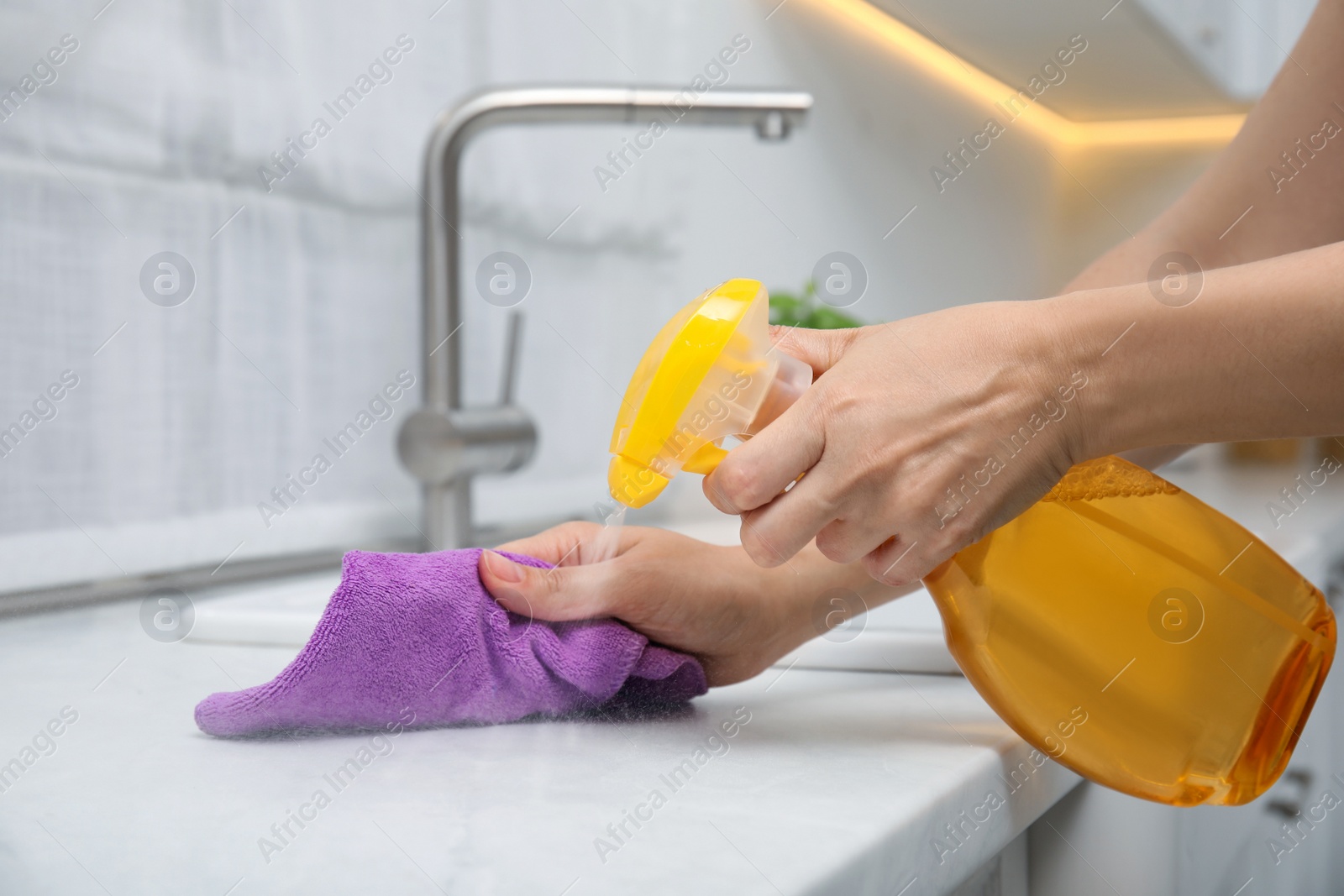 Photo of Woman cleaning white marble countertop with rag and detergent in kitchen, closeup