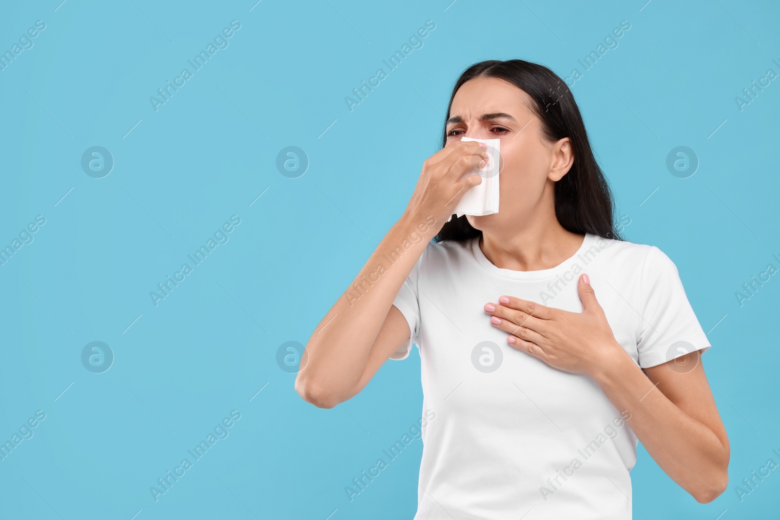 Photo of Suffering from allergy. Young woman blowing her nose in tissue on light blue background. Space for text