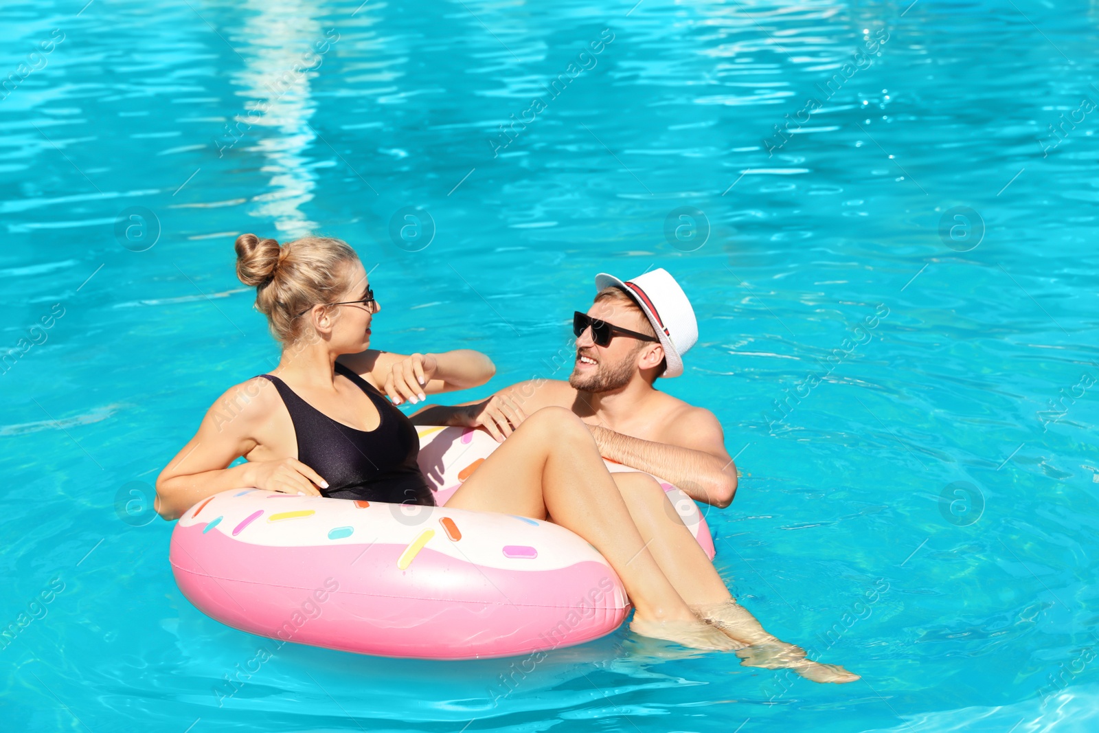 Photo of Happy young couple with inflatable ring in swimming pool