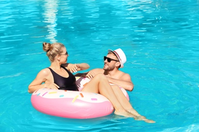 Happy young couple with inflatable ring in swimming pool