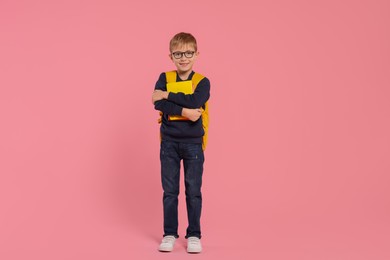 Photo of Happy schoolboy in glasses with backpack and books on pink background