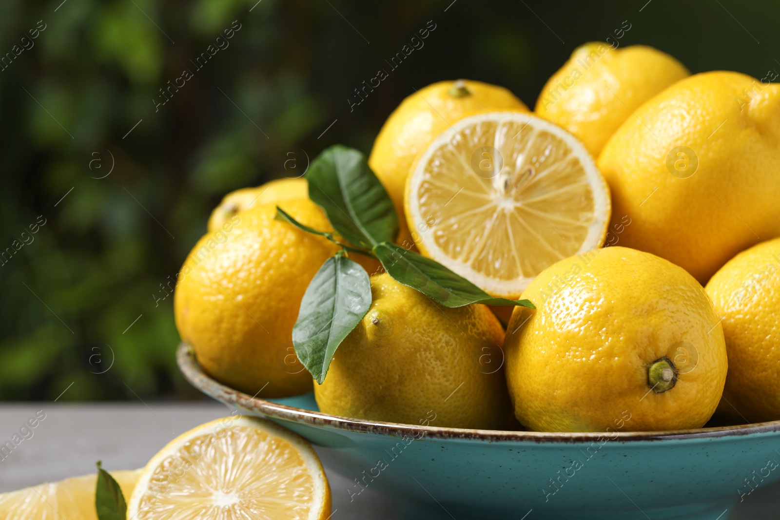 Photo of Fresh lemons and green leaves on grey table outdoors, closeup