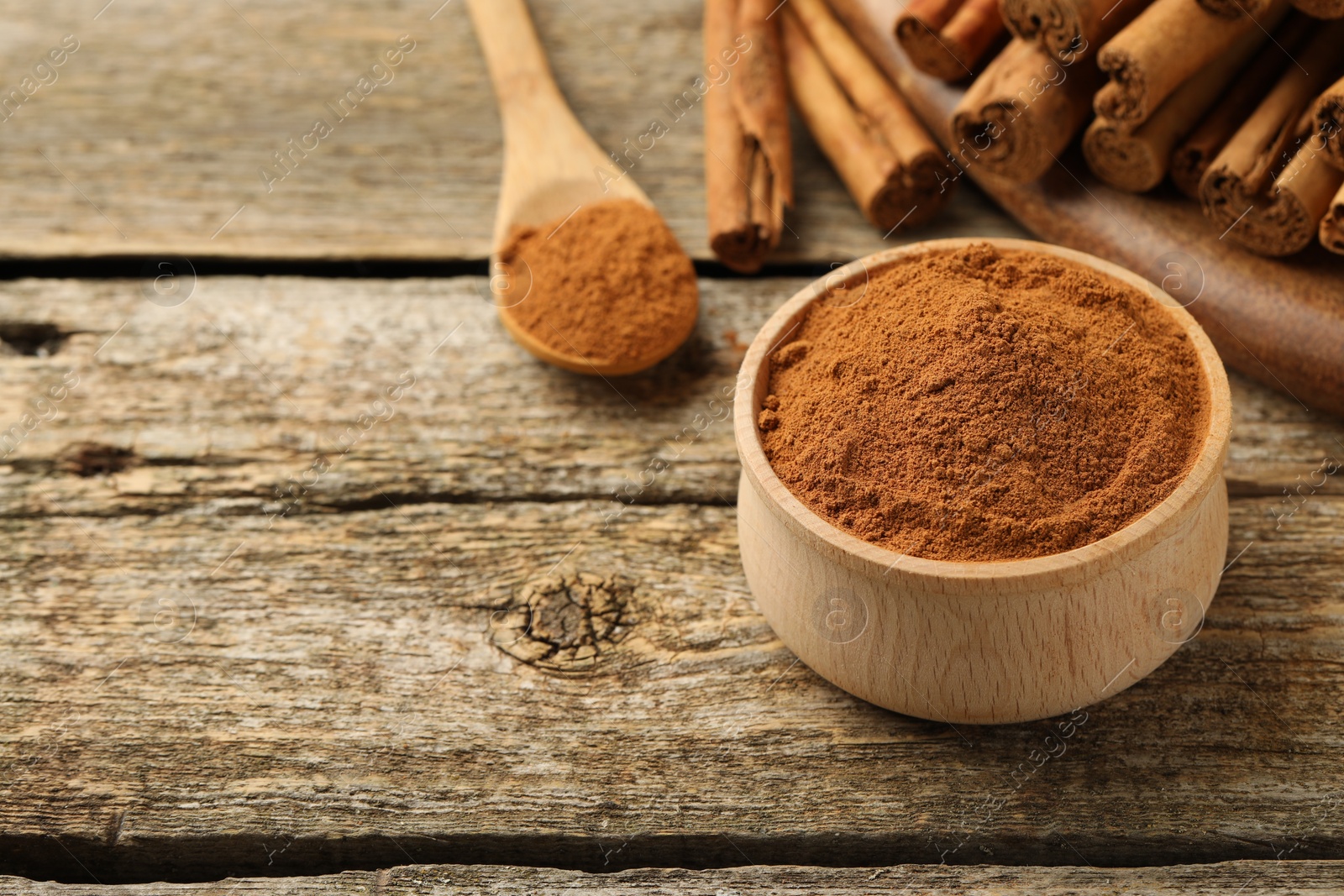 Photo of Bowl of cinnamon powder and sticks on wooden table. Space for text