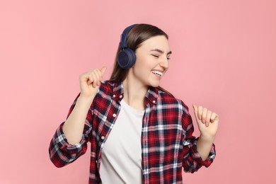 Happy woman in headphones enjoying music and dancing on pink background