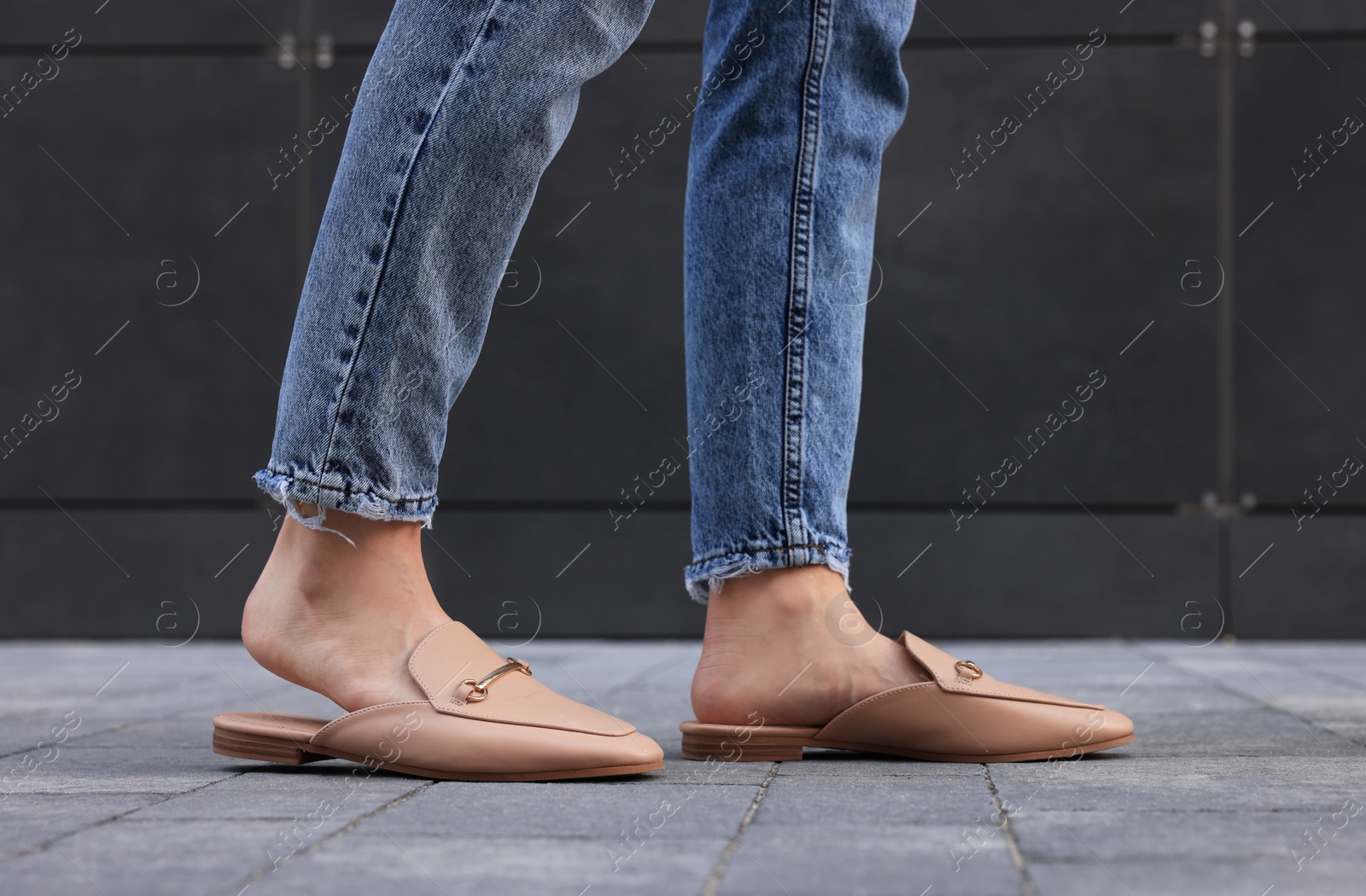 Photo of Woman in blue jeans and fashionable slippers walking on city street, closeup