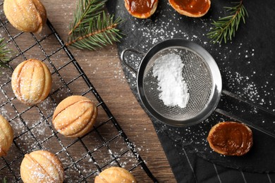 Photo of Delicious nut shaped cookies with powdered sugar and fir branches on wooden table, flat lay