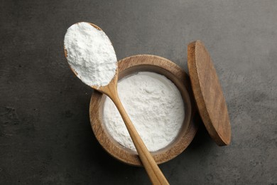 Photo of Baking powder in bowl and spoon on grey textured table, top view