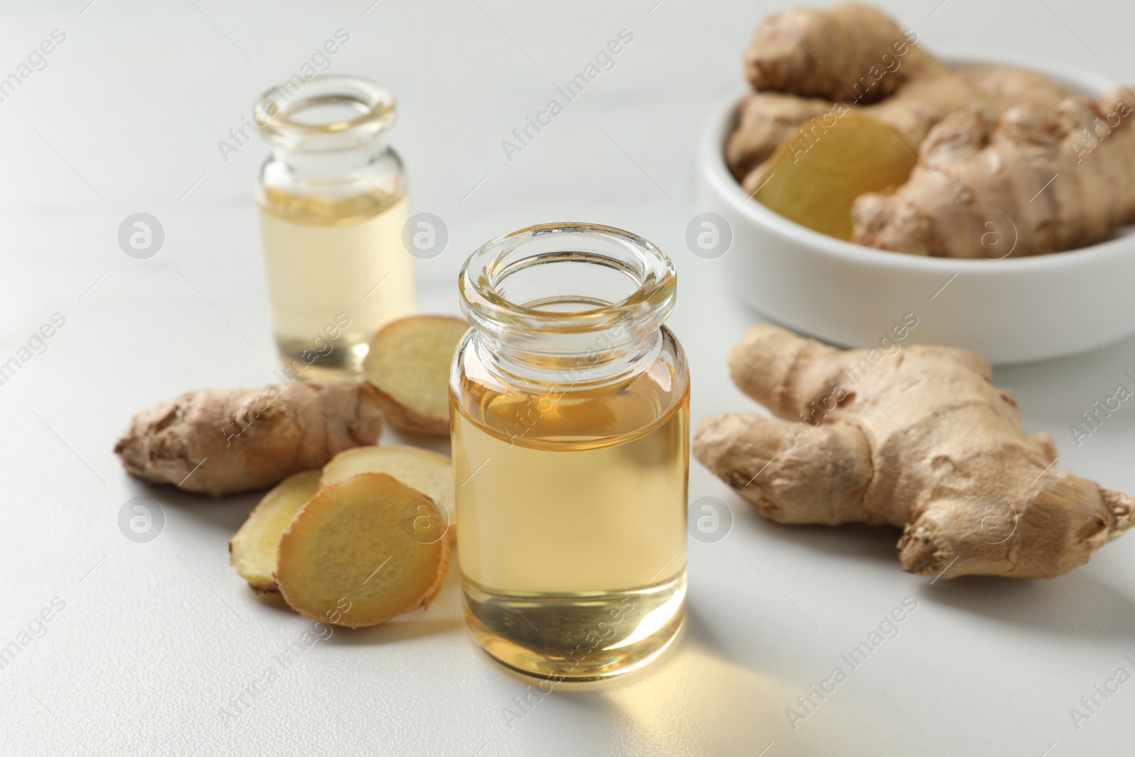 Photo of Glass bottle of essential oil and ginger root on white table