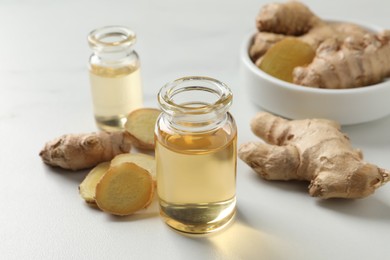 Glass bottle of essential oil and ginger root on white table