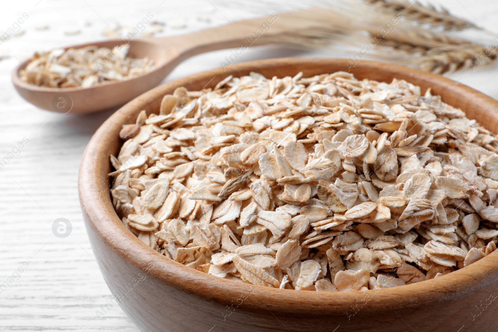 Photo of Oatmeal, bowl and spoon on white table, closeup