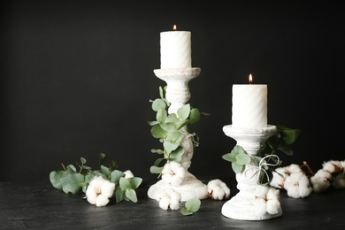Photo of White wooden candlesticks with burning candles and floral decor on black stone table. Space for text