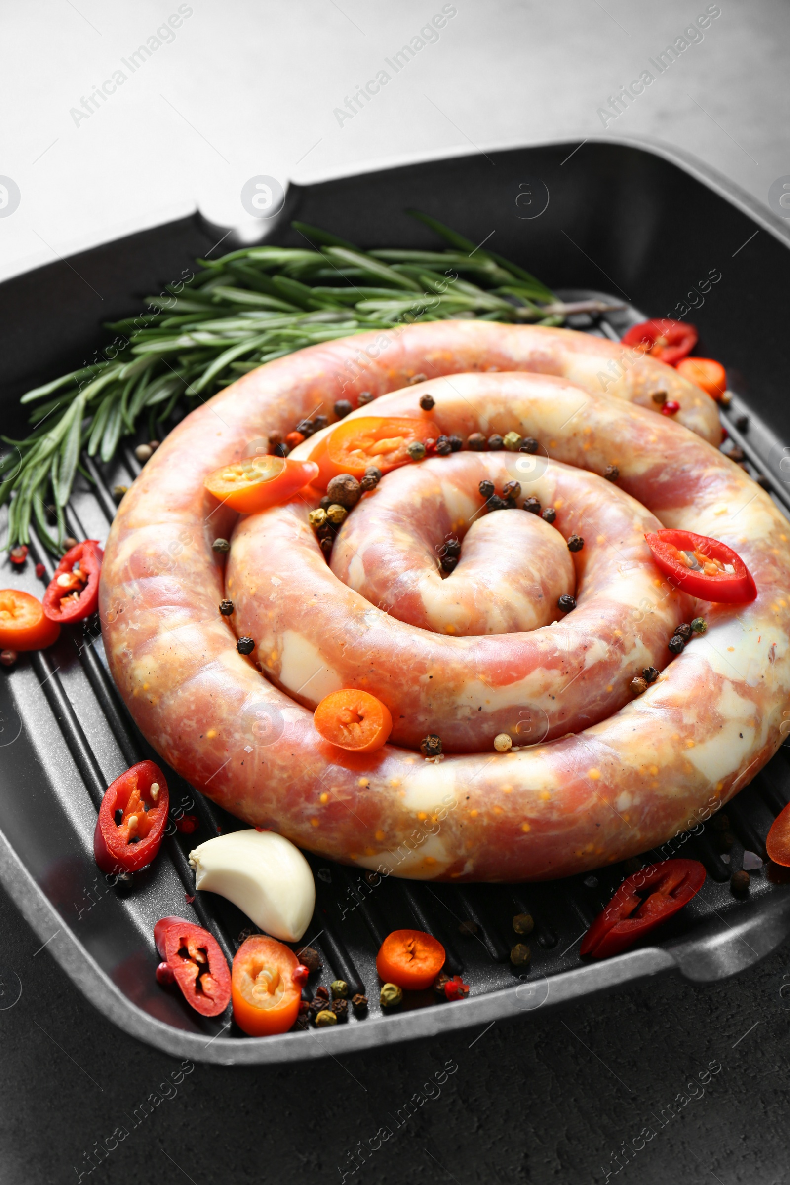 Photo of Pan with raw homemade sausage, chili pepper, garlic and rosemary on grey table, closeup