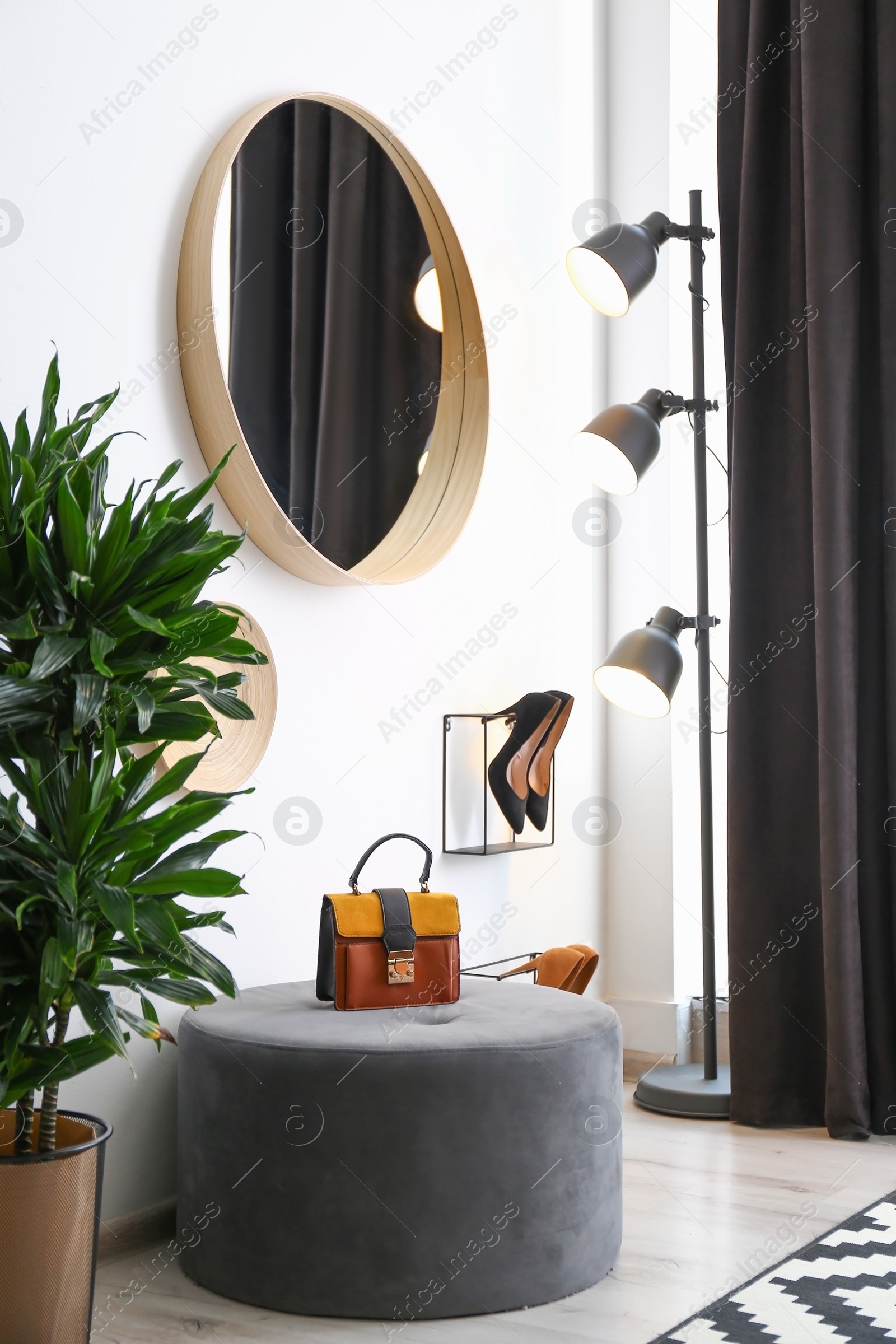 Photo of Hallway interior with big round mirror and ottoman chair near white wall