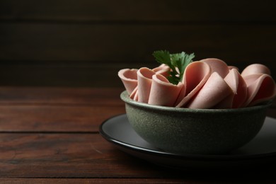 Photo of Slices of delicious boiled sausage with parsley on wooden table, closeup. Space for text