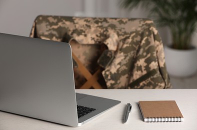 Notebook, laptop and pen on white table indoors. Military education