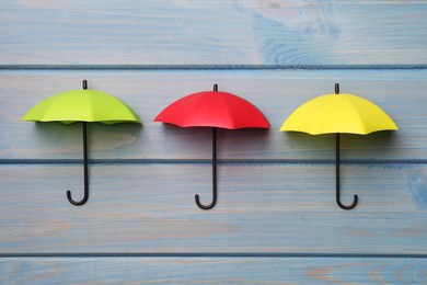 Photo of Small color umbrellas on light blue wooden background, flat lay