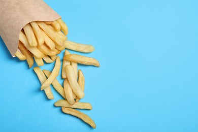 Paper cup with French fries on light blue table, above view. Space for text