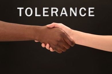 Image of Tolerance, support and cooperation concept. Woman and man of different races shaking hands on black background, closeup