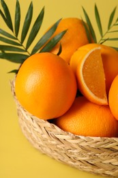 Photo of Fresh oranges in wicker basket on yellow background, closeup