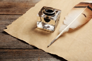 Feather pen, inkwell and blank parchment on wooden table