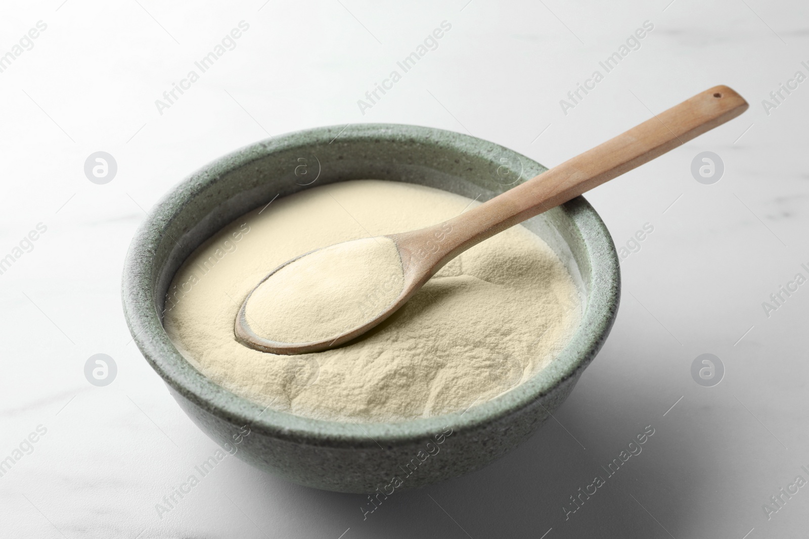 Photo of Bowl and spoon of agar-agar powder on white marble table