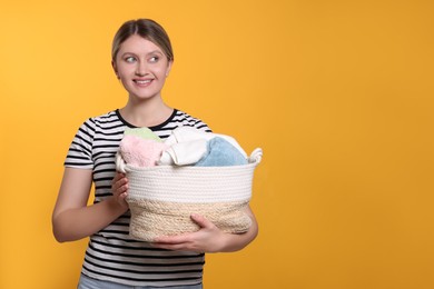 Happy woman with basket full of laundry on orange background. Space for text