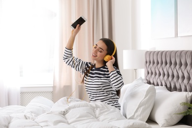Photo of Young woman with headphones and mobile device enjoying music in bed